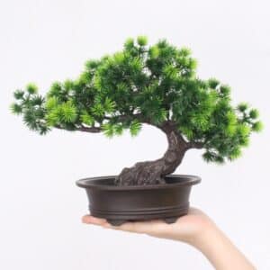 Pianta di pino bonsai artificiale in vaso di plastica, tenuta da una mano.