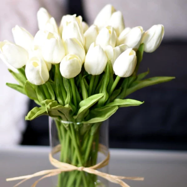 Bouquet di tulipani di plastica beige in un vaso trasparente su un tavolo grigio