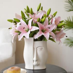 Bouquet di gigli artificiali rosa in un vaso con un volto.