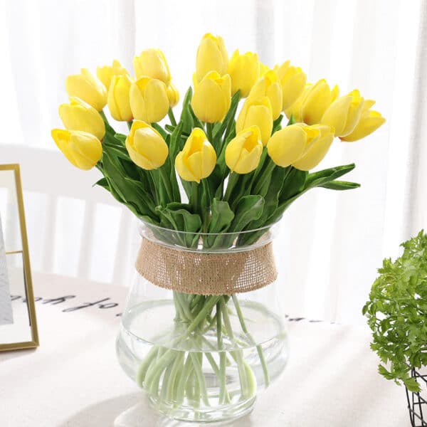 Bouquet di tulipani gialli in un vaso trasparente su un tavolo con una tovaglia bianca