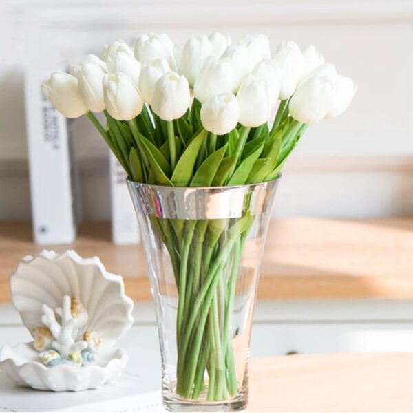 Un bouquet di tulipani bianchi in un vaso trasparente su un tavolo con dei libri alle spalle.