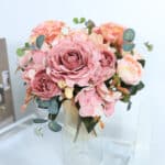 Un bouquet di rose e peonie in stile vintage in un vaso trasparente su un ordine e davanti a una parete bianca.