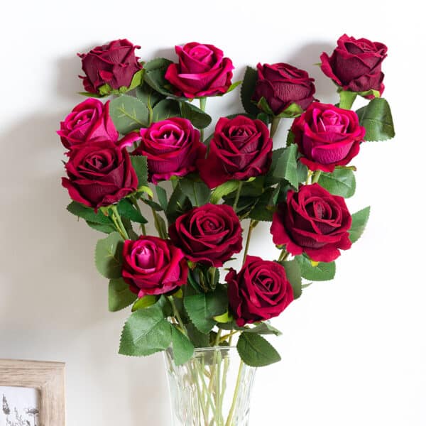 Un bouquet di rose rosse in un vaso trasparente su una parete bianca.