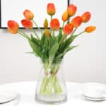 Un bouquet di tulipani arancioni in un vaso trasparente su un tavolo apparecchiato con piatti e una tazza.