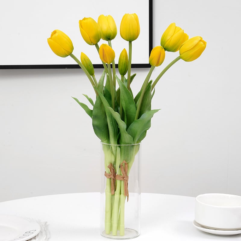 Bouquet di tulipani gialli in un vaso trasparente su un tavolo bianco su sfondo grigio.