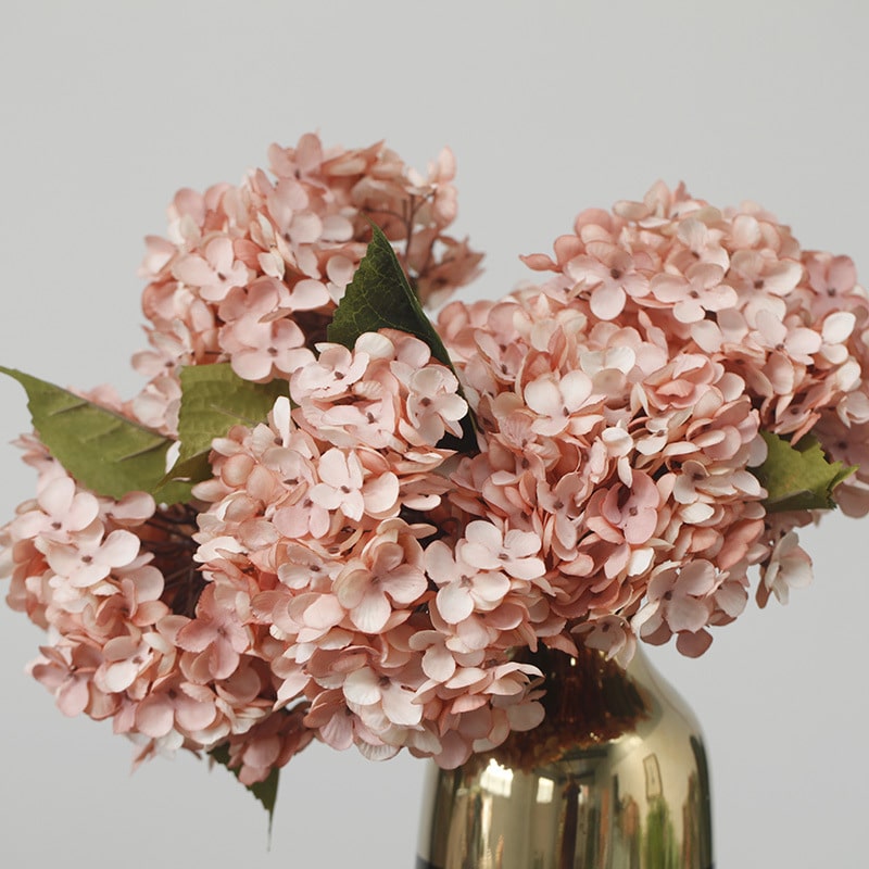 Bouquet di ortensie artificiali rosa in vaso dorato. Sfondo grigio.
