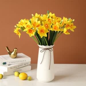 Un bouquet di narcisi gialli in un vaso di terra bianca su un tavolo bianco con libri e limoni.