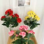 3 mazzi di fiori di geranio artificiali rossi e gialli su un piccolo tavolo di legno