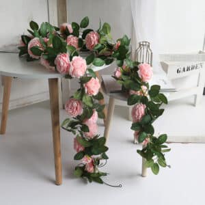 Tre ghirlande di peonie rosa artificiali su un tavolino bianco con gambe in legno scandinavo su un pavimento bianco