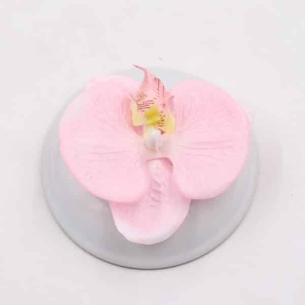 Possiamo vedere un fiore di orchidea rosa molto bello su uno sfondo bianco. È artificiale, ma sembra un fiore vero