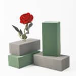 Su uno sfondo bianco, 2 mattoni di muschio verdi e 2 grigi, uno sopra l'altro, con una rosa con fogliame piantata all'interno.