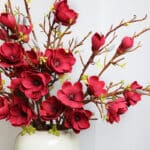 Bouquet di magnolie rosse con rami in un vaso bianco.