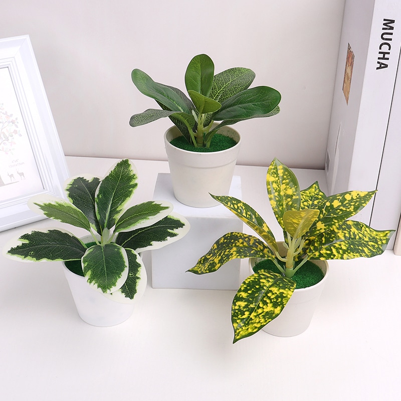 Tre piccole piante verdi artificiali in vasi bianchi su un mobile bianco.