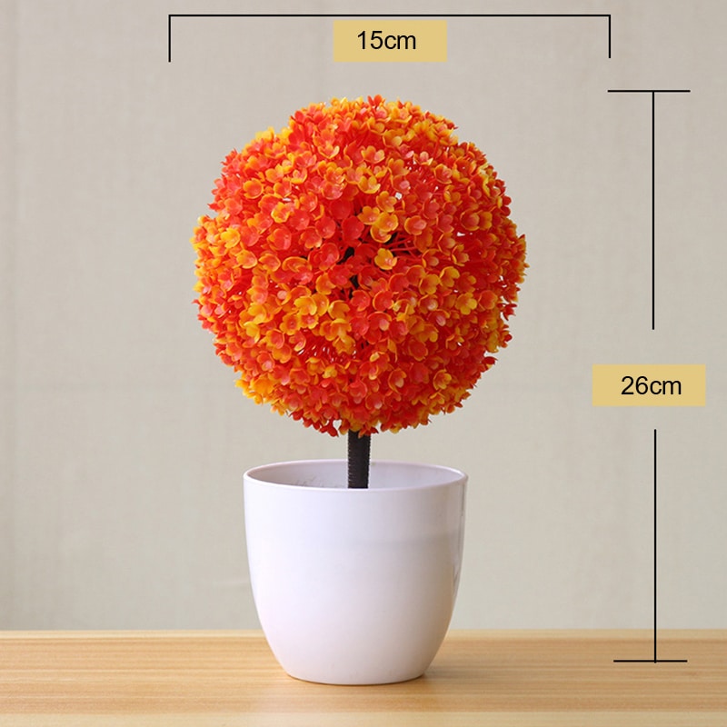 Pianta artificiale in una palla arancione in un vaso bianco.