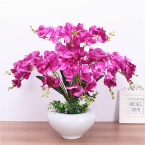 Su un mobile, vediamo un vaso di fiori bianco con all'interno orchidee viola artificiali.