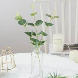 Pianta artificiale di foglie di eucalipto in un vaso su un tavolo bianco