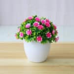 Piccola pianta artificiale in vaso bianco con fiori rosa.