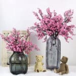 Due vasi contenenti bouquet di fiori di ciliegio. Ci sono anche due orsetti di peluche e uno sfondo bianco.