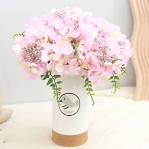 Un bouquet di ortensie rosa in un vaso bianco su un mobile bianco.