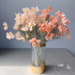 Bouquet di fiori artificiali di geranio bianco e arancione in un vaso su un tavolo grigio