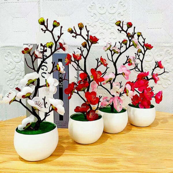 Rami di fiori di ciliegio di diversi colori in vasi rotondi bianchi su un tavolo di legno chiaro davanti a una parete bianca.