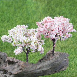 Due ciliegi artificiali di colore bianco e rosa fioriscono su un tronco di legno in mezzo all'erba.